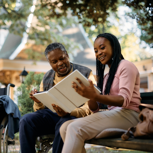 elderly man and his daughter looking at family photo album in park at nursing home