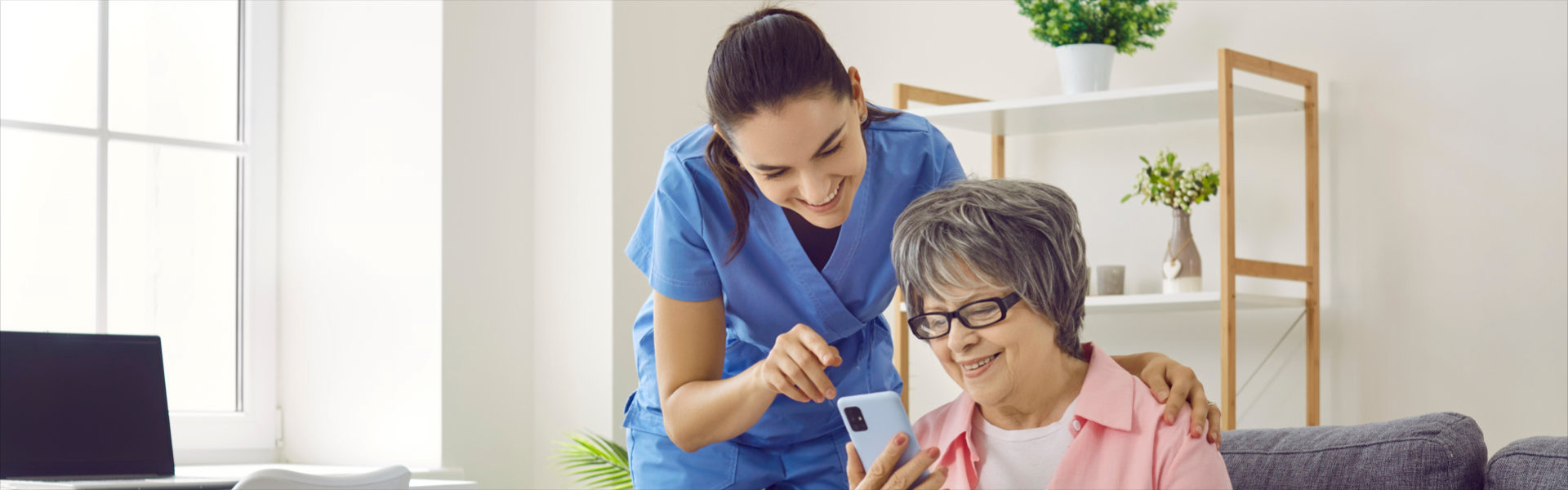 Smiling caregiver and elderly woman in nursing home looking at mobile phone screen together
