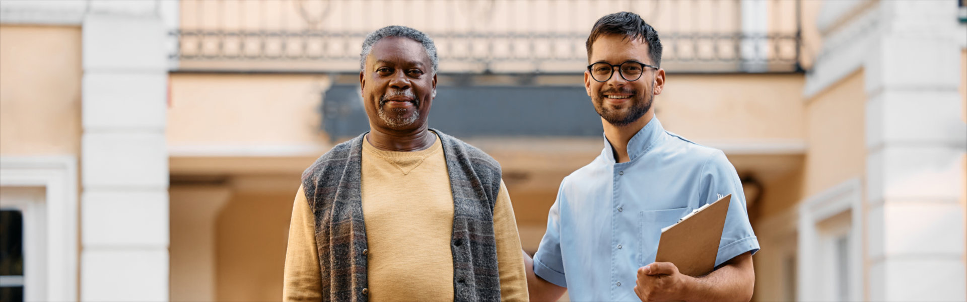 man and young caregiver in front of residential care home looking at camera